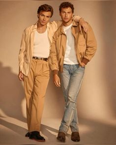 two men standing next to each other in front of a white wall wearing tan clothing