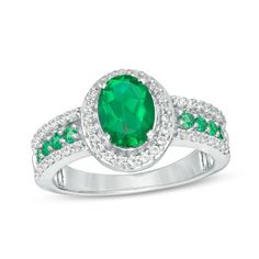 Amp up the fashion volume with this gorgeous fashion ring. Crafted in sterling silver, this resplendent design showcases an 8.0 x 6.0mm oval-shaped lab-created verdant-green emerald wrapped in a shimmering frame of petite lab-created white sapphires. The luxurious shank sparkles with a row of 1.9mm created emeralds bordered in petite created white sapphires. Polished to a bright shine, this choice is a standout style. Custom-made to fit her ring size. Sterling silver rings cannot be resized afte Dazzling Oval Emerald Ring With Accent Stones, Dazzling Green Emerald Oval Ring, Dazzling Oval Green Emerald Ring, Dazzling Green Oval Ring, Dazzling Oval Green Ring, Green Oval Rings With Halo Design, Oval Green Rings With Halo Design, Green Oval Halo Ring For Anniversary, Elegant Green Oval Rings