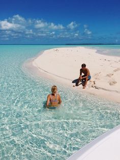 two people sitting on the beach in shallow water