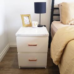 a nightstand with two drawers next to a bed and a lamp on top of it