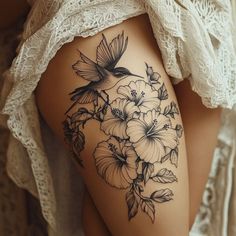 a woman's thigh with flowers and a hummingbird tattoo on her side,