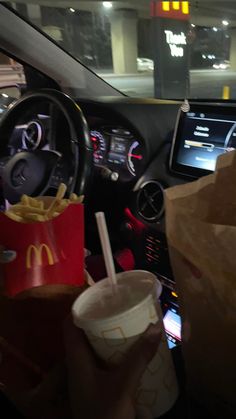 a person sitting in a car holding a drink and some fries with a paper cup next to them