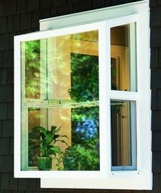 an open window with potted plants in front of it and the reflection of trees outside