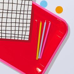 a red tray with two yellow and one pink straws on it next to a white napkin