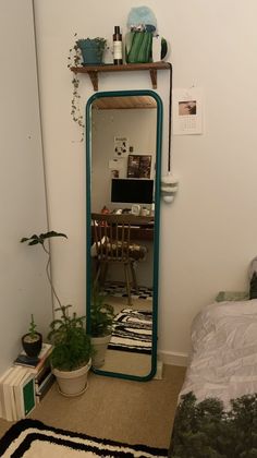 a room with a bed, desk and mirror on the wall next to a plant