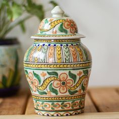 an ornate ceramic jar sitting on top of a wooden table next to a potted plant