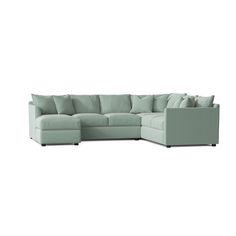 a large sectional couch with pillows on the top and bottom corner, in light green