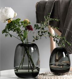 two vases with flowers in them sitting on a table next to a chair and blanket