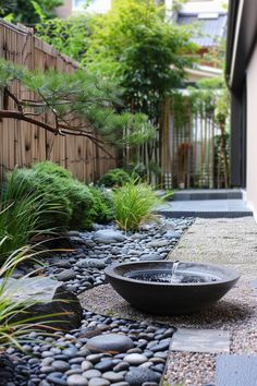 Zen garden with a small black stone water basin, pebbled pathways, and vibrant green plants surrounded by bamboo fencing. Tranquil and serene atmosphere. Zen Garden Side Yard, Long Narrow Garden Ideas Landscaping, Modern Zen Garden Design, Zen Garden With Water Feature, Zen Garden Patio, Japanese Shade Garden, Zen Backyard Landscaping, Interior Zen Garden, Side Garden Ideas Narrow