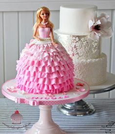 a barbie doll cake sitting on top of a white cake stand next to a cupcake