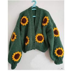 a green knitted sweater with sunflowers on the front and back, hanging from a hook