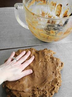 a hand touching a cookie on top of a counter next to a mixing bowl and spatula