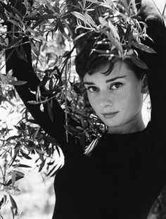 black and white photograph of a woman with her hands on her head, in front of an olive tree