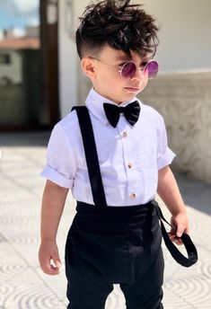 a young boy wearing sunglasses and suspenders with a bow tie in front of a building