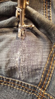 the sewing machine is stitching through the back pocket of a pair of blue jeans