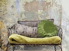 a green pillow sitting on top of a metal bench in front of a dirty wall