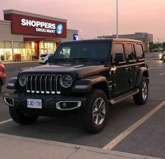 a black jeep is parked in front of a shoppers drive - thru mall at dusk