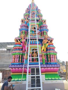 a man standing on top of a ladder next to a giant colorful building with statues