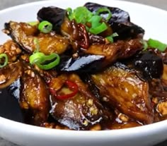 a white bowl filled with cooked eggplant and other food items on top of a table