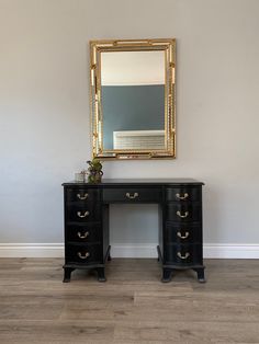 a black desk with two drawers and a gold framed mirror on the wall above it