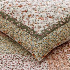 a close up of a quilted pillow on a bed with floral patterns and colors