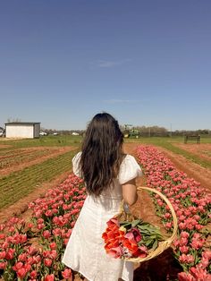 a woman in a white dress holding a basket full of flowers on top of a field