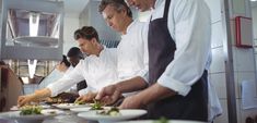 three chefs preparing food in a kitchen with white walls and tile flooring on the wall