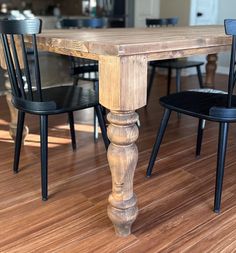 a wooden table sitting on top of a hard wood floor next to two black chairs