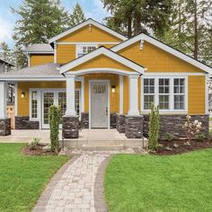 a yellow house with white trim and stone accents in the front yard, along with green grass