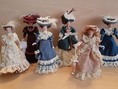 five dolls are lined up in different dresses and hats, all wearing bonnets on their heads