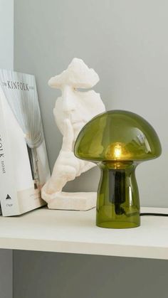 a green mushroom lamp sitting on top of a white shelf next to a book case