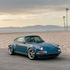 a blue porsche parked on the beach with palm trees in the background