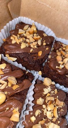 four pieces of chocolate cake with nuts on top in paper trays, ready to be eaten