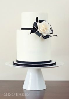 a white and black wedding cake with a flower on top is sitting on a table