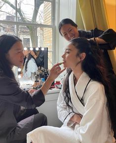 two women are getting their makeup done in front of a window