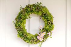 a wreath made out of moss and flowers on a white door with the letter o