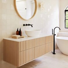 a white bath tub sitting next to a sink under a round mirror in a bathroom