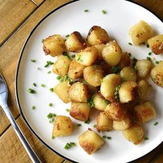 a white plate topped with fried potatoes on top of a wooden table next to a fork