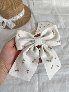 a hand holding a small white bow on top of a bed next to a straw hat