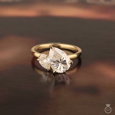 an engagement ring with two pear shaped diamonds on it, sitting on top of a table