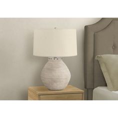 a white lamp sitting on top of a wooden table next to a night stand and bed