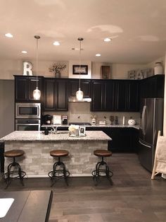 a kitchen with two stools in front of an island and black cabinets on the wall