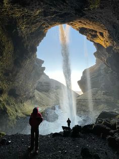 a person standing in front of a cave with water coming out from the entrance to it