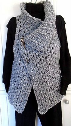 a gray crocheted vest hanging on a white door with a black shirt underneath it