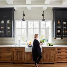 a woman standing in front of a kitchen sink with lots of counter space and cabinets