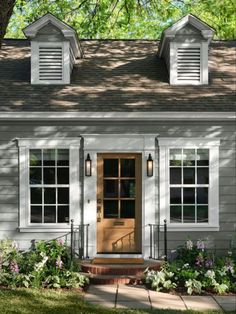 a small gray house with white shutters and a brown door on the front porch