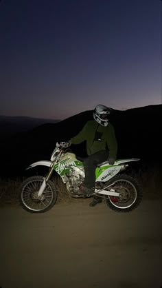 a man riding on the back of a green and white dirt bike in the dark