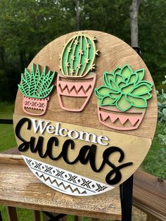 a welcome sign with succulents and cactuses on it in front of some trees