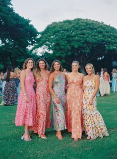 four women in dresses are posing for a photo on the grass at an outdoor event