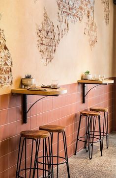 three wooden stools sit in front of a wall with peeling paint on the walls